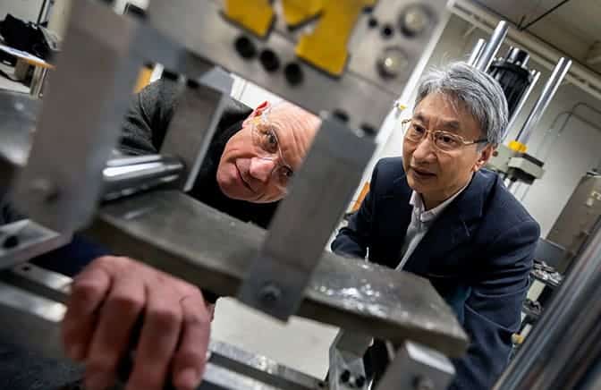 Two people observe a cement tensile test.