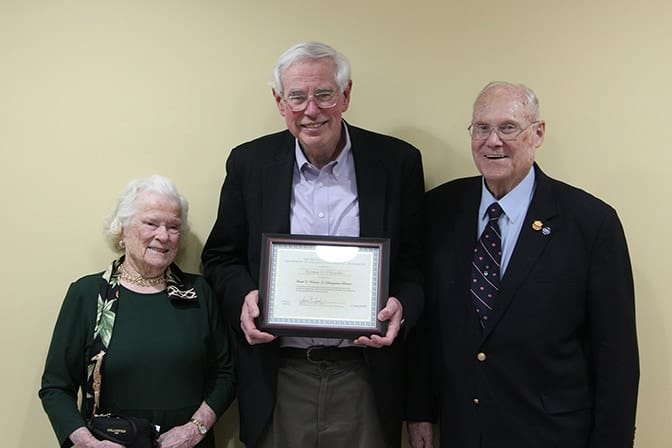 Three people stand, with one holding a plaque