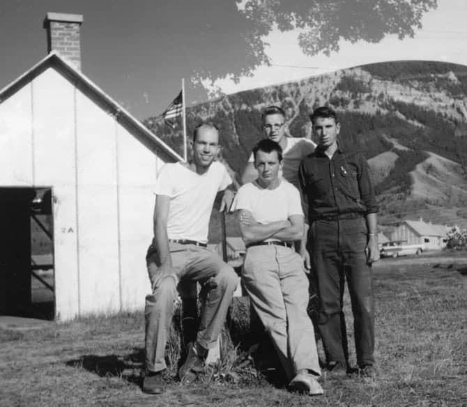 Black and white image of four men in front of wooden building and mountains