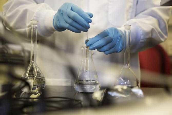 A person works with three chemical flasks containing transparent clear liquid