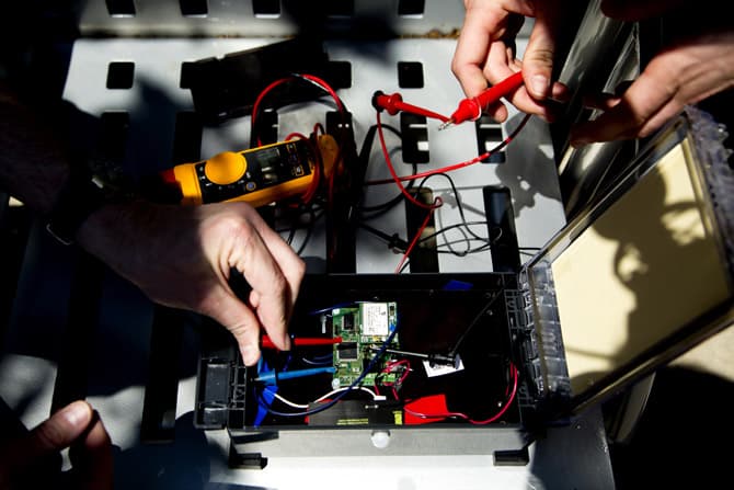 Close-up of two people working on a small box of wired sensors