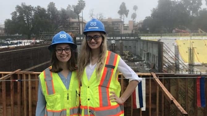 Two people in safety vests and hard hats standing in front of a construction site.