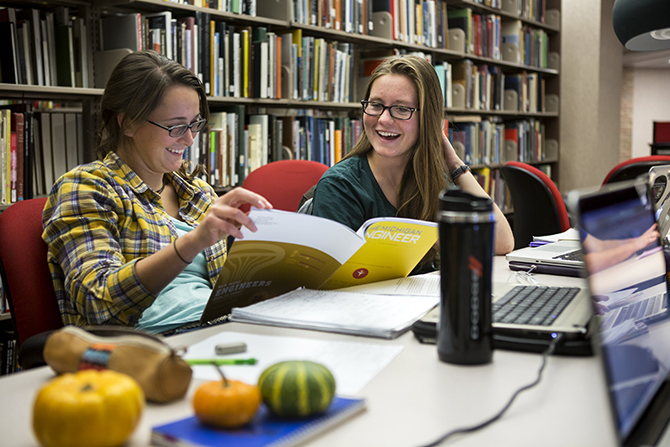 Two students read The Michigan Engineer Magazine Overlaid with badges highlighting US News and World Report rankings