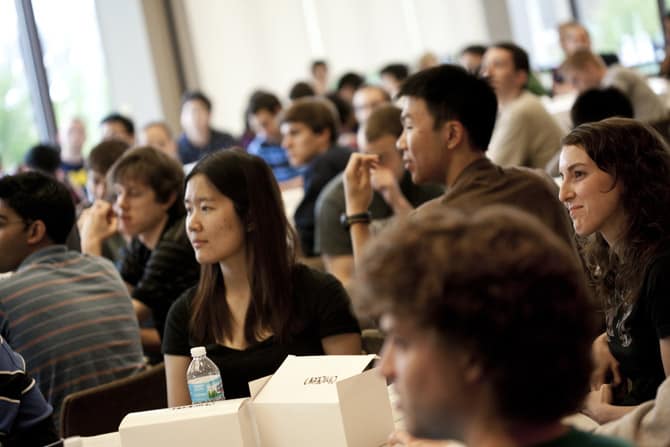 A room full of people seated at round tables, looking towards a point out of view