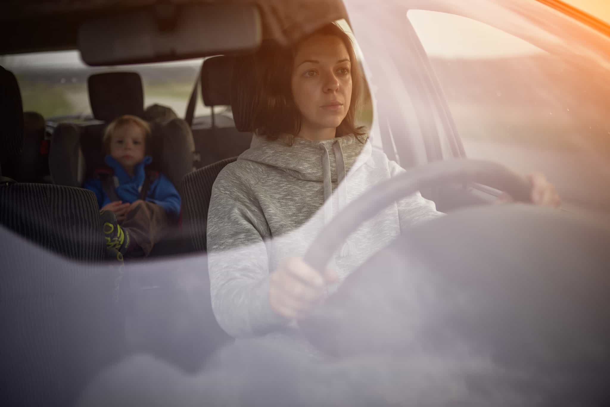 Mother drives a car, a child in a safety seat in the rear seat